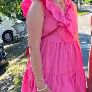 Rosa klänning med volangdetaljer - Säljer en superfin rosa klänning med volanger och öppen rygg. Perfekt för sommarens fester eller en mysig dag i solen. Klänningen är ärmlös och har en luftig passform som gör den bekväm att bära hela dagen. Den knyts i ryggen för en extra söt detalj. Passar perfekt för en somrig look! 🌸 Öppen och ärlig att den är köpt på shein för flera år sedan. Nu säljer jag den då den har blivit för liten:(