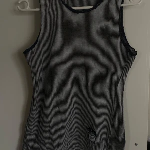 Randig ärmlös topp från D&G - Snygg och stilren topp från D&G i mörkblått och vit randigt mönster. Perfekt för sommardagar. Toppen har en enkel design med en liten logga längst ner. Spetsdetalj runt armhålan och kragen. Passar som både pyjamas (skönt material) och som topp till ett par jeans eller shorts! Storlek M men passar både som S/M. Har en liten fläck på vänster bröst, syns inte så mycket på. Bomull 95% och Elastan 5%. 