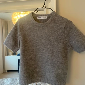 Grå stickad tröja från Zara - Säljer en supermysig grå stickad tröja från Zara. Den har korta ärmar och en klassisk rund halsringning. Perfekt för både höst och vår när du vill ha något bekvämt men ändå stilrent. Passar till både jeans och kjol!