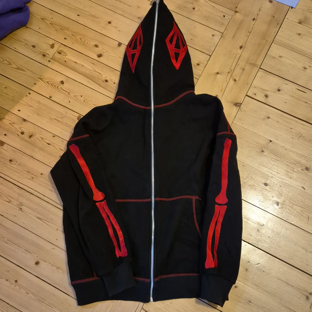 Cool svart hoodie med röda skelettdetaljer på ärmarna och huvan. Röda sömmar. Storlek small. Nyskick. Minns ej märke, men köpt från England. . Tröjor & Koftor.