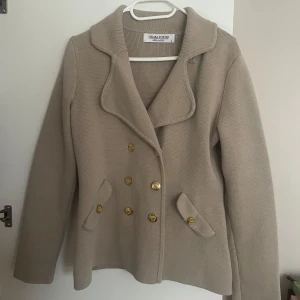 Beige kofta från Chiara Forthi - Säljer en stilren beige kappa från Chiara Forthi i 100% bomull. Storlek L men passar mig som har S/M! Bra material, varm tröja.  Den har en dubbelknäppt design med snygga guldknappar och långa ärmar. Perfekt för höst och vår när du vill se både elegant och avslappnad ut. Passar till både vardag och fest!