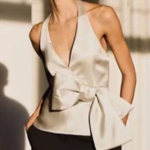  Champagne färgad topp från Zara - Säljer en superfin champagne färgad halterneck topp i satin, perfekt för nyår. Den har en stor rosett i midjan och en v-ringad design. Den har små fläckar där fram som syns på bilden, som man säkert kan försöka få bort🫶