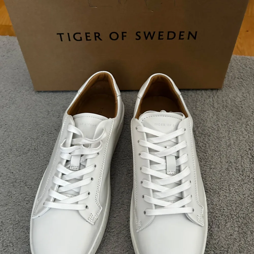 Säljer ett par stilrena vita sneakers från Tiger of Sweden i skinn. De har en klassisk design med snörning och en bekväm passform. Perfekta för både vardag och festliga tillfällen. Skorna är i nytt skick och kommer i originalförpackning. Ifall frågar så är det bara att skicka ett meddelande. . Skor.