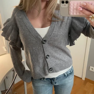 Kofta med volanger - Grå kofta med volangdetaljer på ärmarna, bra skick använd fåtal gånger