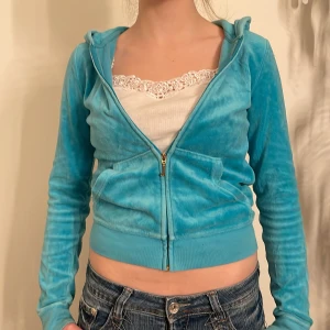 Turkos velourjacka från Juicy Couture - Säljer en snygg turkos velourjacka från Juicy Couture. Den är croppad med dragkedja och har en cool broderad design med rosa blommor och diamantdetaljer på ryggen. Alla stenar är kvar