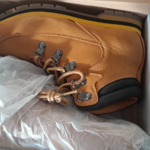 Gula kängor från Warp - Säljer ett par snygga och robusta kängor från Warp i mörkgul färg. De har snörning och en rejäl sula som ger bra grepp. Perfekta för höst- och vinterväder. Helt nya i kartong!