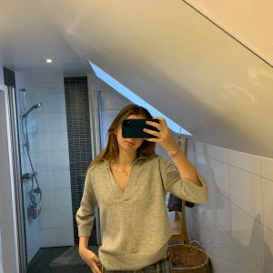 Grå tröja från H&M - Mysig grå tröja från H&M i storlek S. Den har en djup v-ringning och en avslappnad passform med korta ärmar. Perfekt för kyliga dagar och att mysa i hemma. Tröjan är i bra skick och gjord av ett mjukt material som känns skönt mot huden.