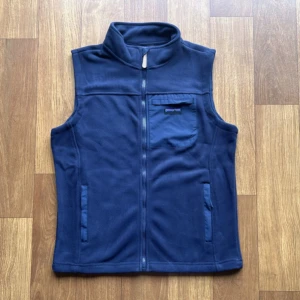  fleeceväst från Patagonia - Säljer en snygg blå fleeceväst från Patagonia i mycket bra skick. Västen har en dragkedja framtill och en praktisk bröstficka med logga. Perfekt för lager-på-lager under höst och vår. Storlek är herr M. Vid funderingar hör gärna av er