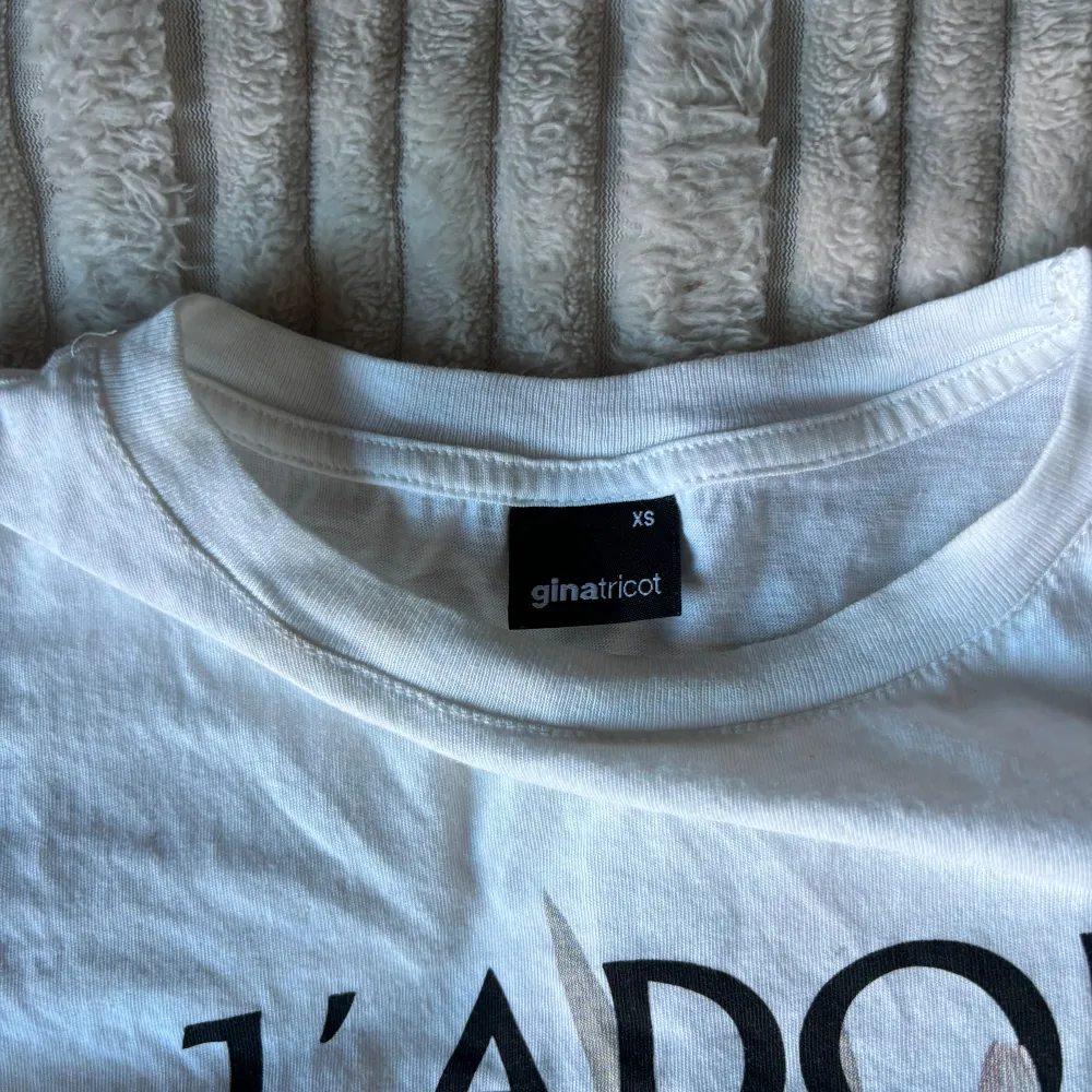 Säljer en superfin vit t-shirt från Gina Tricot i storlek XS. Den har ett tryck med texten 'J'ADORE' och ett vackert blommotiv i mjuka färger. Perfekt för en avslappnad look eller att styla upp med en snygg jacka. T-shirten är i bra skick och gjord av mjukt bomullsmaterial.. T-shirts.