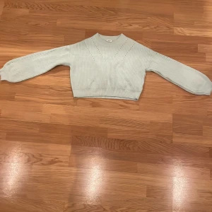 Ljusblå stickad tröja - Säljer en ljusblå stickad tröja. Den har ett snyggt hålmönster och ribbade kanter. Tröjan är långärmad och croppad, perfekt för både vår och höst. Observera en liten fläck på ena ärmen. Passar bra till jeans eller kjol för en avslappnad look.