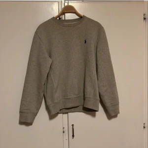 Grå sweatshirt från Polo Ralph Lauren - Säljer en stilren grå sweatshirt från Polo Ralph Lauren i storlek S. Tröjan är i bomull och polyester, perfekt för både höst och vår. Den har långa ärmar och en liten broderad logga på bröstet. Superbekväm och lätt att matcha med allt! 🩶