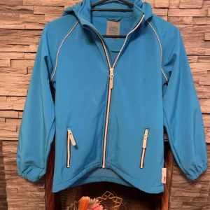 Blå vindjacka från Name It - Säljer en blå vindjacka från Name It i storlek 146. Jackan har en praktisk dragkedja och huva, perfekt för blåsiga dagar. Den är i bra skick och har elastiska muddar vid ärmsluten. Perfekt för vår och höst!