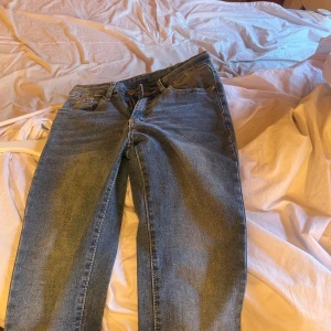Blå jeans med broderad bakficka - Säljer ett par snygga blå jeans i bra skick. De har en broderad detalj på bakfickan och en klassisk femficksdesign. Perfekta för vardagsbruk och kan matchas med det mesta. Passformen är normal och de är midwaist. Perfekt för höst och vår!