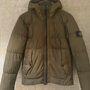  Stone Island puffer  - Säljer en olivgrön dunjacka från Stone Island i mycket bra skick. Jackan har en quiltad design med dragkedja och huva. Perfekt för höst och vinter. Nypris på denna jacka ligger runt 10 000kr mitt pris 3500r pris går att diskutera vid snabb affär. Fraktas direkt! Skriv för fler frågor och bilder