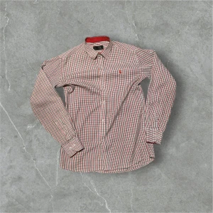 Rutig skjorta från Polo Ralph Lauren - Snygg rutig skjorta från Polo Ralph Lauren i rött, blått och vitt. Perfekt för både vardag och fest! Skjortan har långa ärmar och knappar hela vägen ner. Klassisk krage och en liten broderad logga på bröstet. Passar bra till jeans eller chinos för en stilren look.