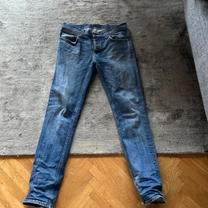 Blå jeans från Nudie Jeans - Säljer ett par snygga blå jeans från Nudie Jeans. De har en klassisk femficksdesign och är i bra skick med en cool tvättad look. Perfekta för vardagsbruk och passar till det mesta. Sköna och stilrena, ett måste i garderoben! Ända dåliga är att fram fickorna är söndriga men går att fixa hyfsat lätt