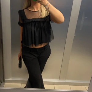 Svart transparent blus - Säljer en svart transparent blus med volangdetaljer. Den har korta ärmar och en luftig passform, perfekt för en festlig kväll. Blusen är i mycket bra skick och ger en elegant look med sitt skira material. Använd fåtal gånger 