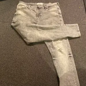 Säljer ett par grå jeans från FSBN i bra skick. De har en snygg, tvättad look med en liten reva på ena benet för en cool touch. Perfekta för vardagsbruk eller en avslappnad utekväll. Midjan är normal och passformen är slim, vilket ger en modern och stilren siluett.