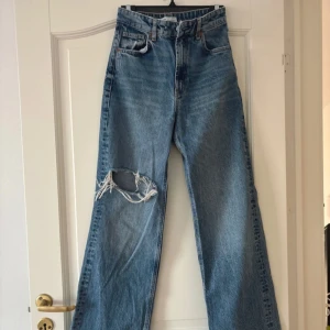 Blå jeans med slitning - Säljer ett par högmidjade jeans med revor från Zara, i mycket bra skick eftersom de knappt är använda