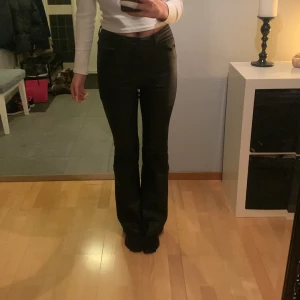 Svarta högmidjade byxor - Säljer ett par snygga svarta skinnbyxor i högmidjad modell. De har en bootcut-stil. Perfekta för både vardag och fest!
