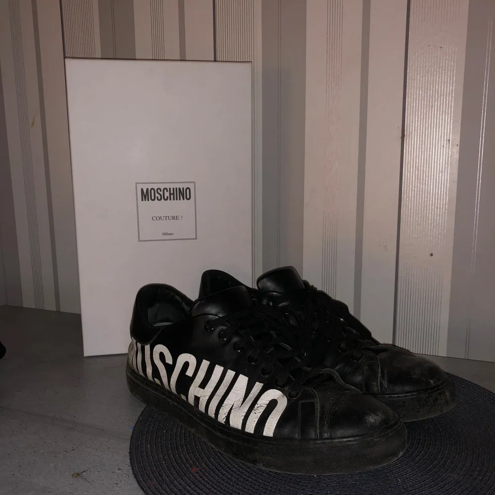 Säljer ett par svarta Moschino sneakers i skinn med stort vitt Moschino-tryck på sidan. Skorna har snörning och är i bra skick. Perfekta för en stilren look med en touch av lyx. Kommer med originalkartong. Nypris runt 3000kr🙌. Skor.