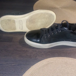 Svarta sneakers från Lanvin - Säljer ett par stilrena svarta sneakers från Lanvin. De har en snygg kombination av skinn och syntet med en vit sula. Skorna har snörning och är i bra skick, perfekta för både vardag och fest.  Priset är inte fast i sten och kan diskuteras. Hör av er vid minsta detalj.