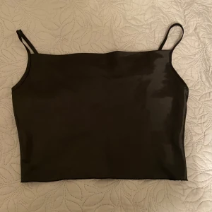 Svart satinlinne - Snyggt svart linne i satinmaterial med smala axelband. Perfekt för en utekväll eller fest. Linnet har en enkel och stilren design som gör det lätt att matcha med olika outfits.