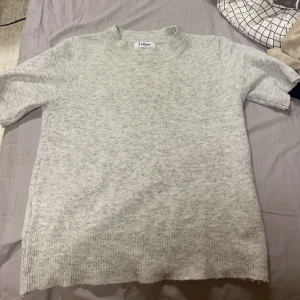 Grå stickad tröja  - Säljer en supermysig grå stickad tröja. Perfekt för kyliga dagar med sin mjuka och bekväma passform. Tröjan har korta ärmar och en klassisk rund halsringning. Passar både till vardags och lite finare tillfällen. Passar både xs och s🩶