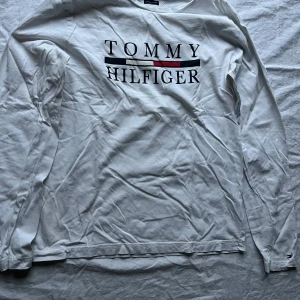 Vit långärmad tröja från Tommy Hilfiger - Säljer en vit långärmad tröja från Tommy Hilfiger i ekologisk bomull. Den har en klassisk design med logotypen tryckt på framsidan. Perfekt för en avslappnad stil och passar till alla säsonger. Tröjan är i bra skick. Perfekt för vardagsbruk!