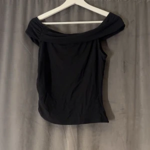 Svart offshoulder topp - Snygg svart offshoulder topp i mjukt material. Perfekt för en utekväll eller fest. Toppen har en elegant och stilren design som passar till många olika outfits.