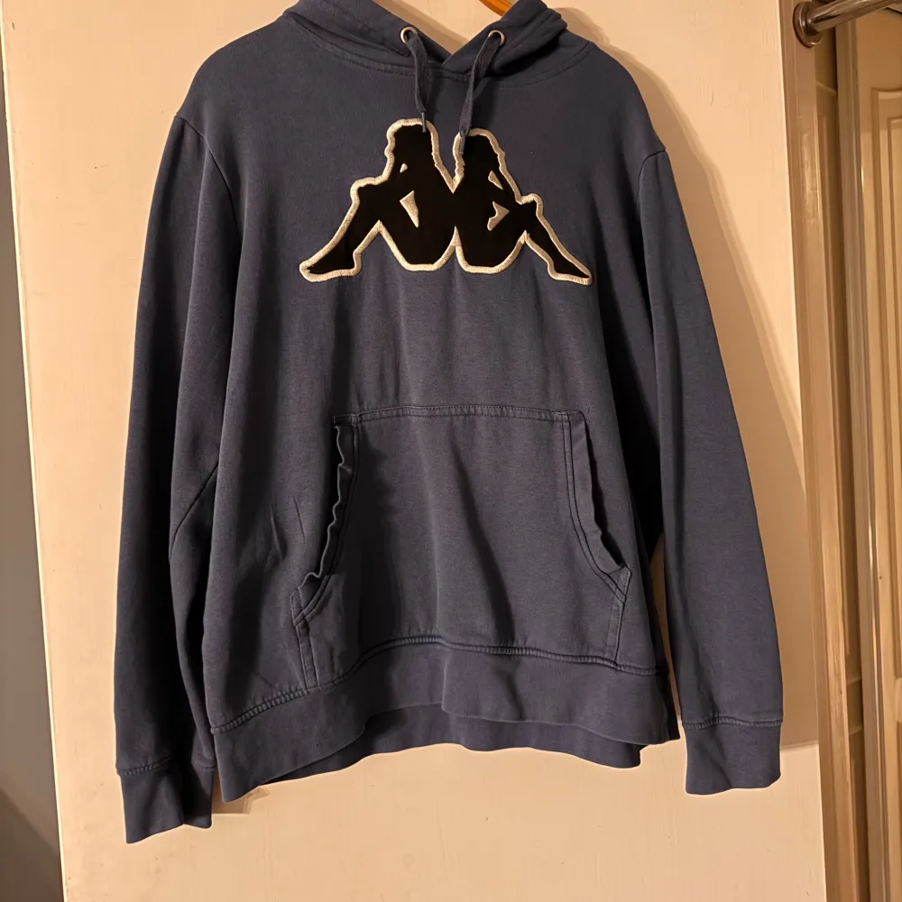 Säljer en snygg mörkblå hoodie från Kappa med det klassiska logotyptrycket på bröstet. Den har en stor ficka fram och justerbar huva med dragsko. Passar perfekt till hösten! Herr modell men passar både killar o tjejer . Hoodies.