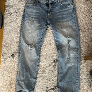 Slitna jeans från Woodbird - Säljer ett par feta, slitna jeans från Woodbird i storlek 33/32. De har en ljusblå tvätt med snygga slitningar och en klassisk femficksdesign. Perfekta för en avslappnad och trendig look. Passar både till vardags och fest! 