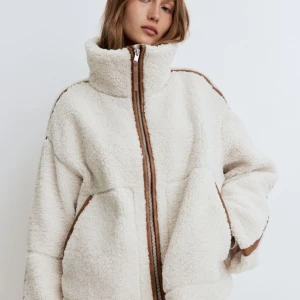 Vit teddyjacka från H&M - Mysig vit teddyjacka från H&M i storlek L. Jackan har en dragkedja framtill och bruna detaljer längs med dragkedjan och axlarna. Perfekt för kyliga höst- och vinterdagar. Den är supermjuk och har en avslappnad passform. Ett måste för garderoben!