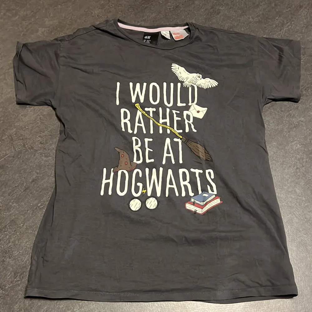 Säljer en svart t-shirt från H&M med texten 'I would rather be at Hogwarts' och  detaljer som en uggla, kvast och böcker. Perfekt för alla Harry Potter-fans! T-shirten är andrig använd, jätte bra skick och har en normal passform. 🧙. T-shirts.