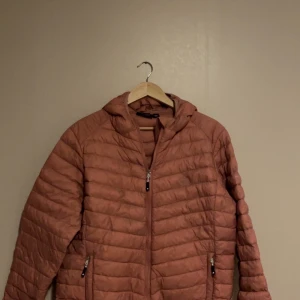 Rosa pufferjacka från Tuxer - Säljer en snygg rosa pufferjacka från Tuxer i storlek XXL. Jackan har en dragkedja framtill och praktiska fickor med dragkedjor. Perfekt för kyliga dagar med sin varma och bekväma design. Huvan ger extra skydd mot väder och vind. Passar perfekt för både höst och vår! 