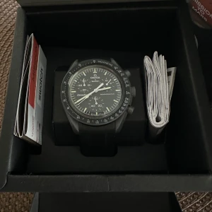  Omega x Swatch Speedmaster MoonSwatch  - Säljer en stilren svart Omega x Swatch Speedmaster MoonSwatch mission to Mercury. Den kommer i originalförpackning med manualer, äkthetsintyg samt påsen. Originalband medföljer. Just nu sitter det ett gummiarmband på klockan som köptes för 600kr. 