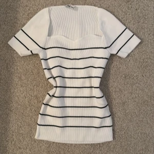 Vit och svart randig tröja  - Säljer en superfin vit tröja med svarta ränder. Den är kortärmad och har en tight passform som framhäver figuren. Perfekt för både vardag och fest! Materialet känns mjukt och stretchigt, vilket gör den bekväm att bära hela dagen.