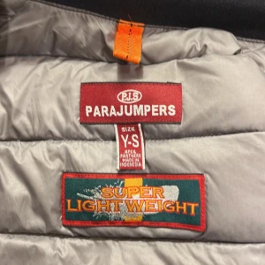 Svart dunjacka från Parajumpers - Säljer en superlätt svart dunjacka från Parajumpers i mycket bra skick. Jackan har en dragkedja framtill och en hög krage med en gul detalj. Perfekt för höst och vår, med en stilren och modern look. Passar bra till både vardag och lite finare tillfällen.passar folk mellan 145-155