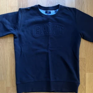 Svart sweatshirt från GANT - Säljer en stilren navy sweatshirt från GANT i mycket bra skick. Tröjan har en broderad logga på bröstet och är tillverkad i ett mjukt material. Perfekt för både vardag och avslappnade tillfällen. Passar ungdomar i storlek 158/164 cm.