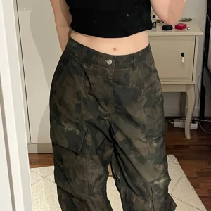 Camouflage cargobyxor - Säljer ett par grymma camouflage cargobyxor i loose fit. Perfekta för en avslappnad stil med praktiska fickor på sidorna. Byxorna är i mörkgrön färg och har även snören så man kan knyta längst ner. Mycket bra skick!😇💕