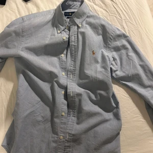 Ljusblå skjorta från Ralph Lauren - Säljer en stilren ljusblå skjorta från Ralph Lauren i storlek S. Skjortan är i slim fit och har klassiska knappar framtill. Perfekt för både vardag och festliga tillfällen. Den är i mycket bra skick och redo för en ny ägare!