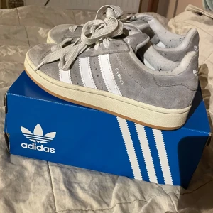 Grå Adidas Campus sneakers - Säljer ett par grå Adidas Campus sneakers i mycket bra skick. De har en klassisk design med vita ränder och snörning. Skorna är gjorda i mocka och har en bekväm gummisula. skriv vid funderingaf❤️