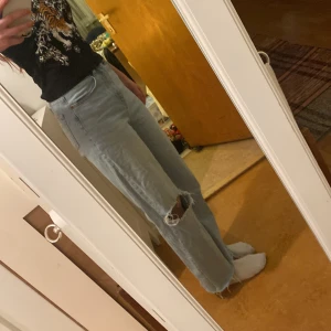 Ljusa jeans med hål - Säljer ett par ljusa jeans i mycket bra skick. De är högmidjade och har en cool slitning på ena benet. Byxorna har en loose passform och är perfekta för en avslappnad stil. De är i jeansmaterial och passar bra till både vardag och fest.