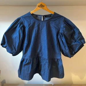 Blå blus från Selected Femme - Säljer en snygg blå blus från Selected Femme i storlek 40. Blusen har puffiga trekvartsärmar och en lös passform med en volangdetalj nedtill. Perfekt för både vardag och fest! 💙