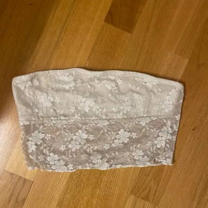 Vit spets tubtopp - Säljer en superfin vit tubtopp i spets. Perfekt för sommaren eller en festkväll! Den är axelbandslös och har ett vackert blommönster. Toppen är i bra skick och passar perfekt till både kjol och byxor.