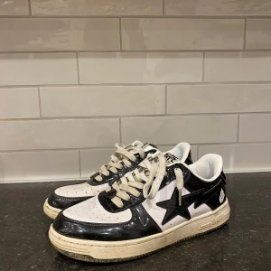 Svartvita sneakers från Bape - Säljer ett par Bape sneakers i svart och vitt. De har en cool stjärndetalj på sidan och klassisk snörning. Skorna är i bra skick med lite slitage på sulan. Perfekta för vardagsbruk eller att ge din outfit en streetwear-känsla.