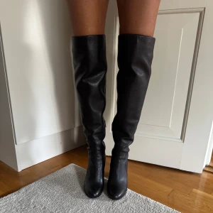 Svarta stövlar från Michael Kors - Snygga svarta stövlar i skinn från Michael Kors. De är knähöga med en bekväm klack och har en dragkedja på sidan för enkel på- och avtagning. Perfekta för höst och vinter, både till vardags och fest. Stilrena och tidlösa, dessa stövlar är ett måste i garderoben!