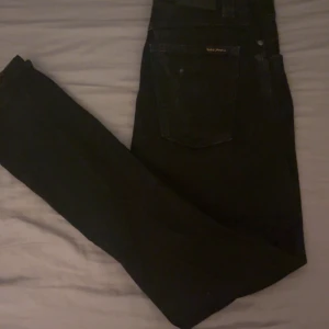 Svarta Nudie jeans grim trim - Säljer ett par svarta jeans från Nudie Jeans i mycket bra skick. Har inte använt dom så mycket då dom bara har legat i min garderob så jag lägger ut dom då nån annan kanske har användning av dom. Jag är runt 175cm och de sitter bra på mig. De sitter som slim jeans alltså lite tajtare. Storleken är W31 och L32