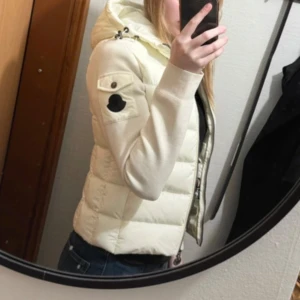 Off white dunjacka från Moncler - Säljer en snygg beige dunjacka från Moncler i mycket bra skick. Jackan har en dragkedja och en mysig huva, perfekt för kyliga höst- och vinterdagar. Den är långärmad och har en stilren design med en liten logga på ärmen. Superfin och varm, perfekt för att hålla stilen i kylan!