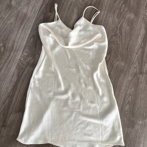Vit axelbandslös klänning - Säljer en elegant vit klänning med smala axelband och en draperad halslinje. Små trådar har åkt ut från klänningen därav priset 